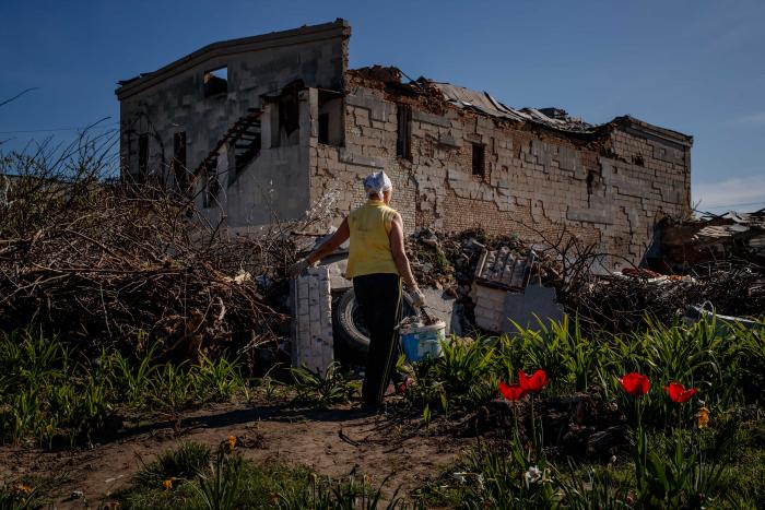Nina cuida las flores de su jardín frente a su casa destruida por proyectiles de alto calibre, el 6 de mayo de 2022, en Baryshivka (Ucrania).