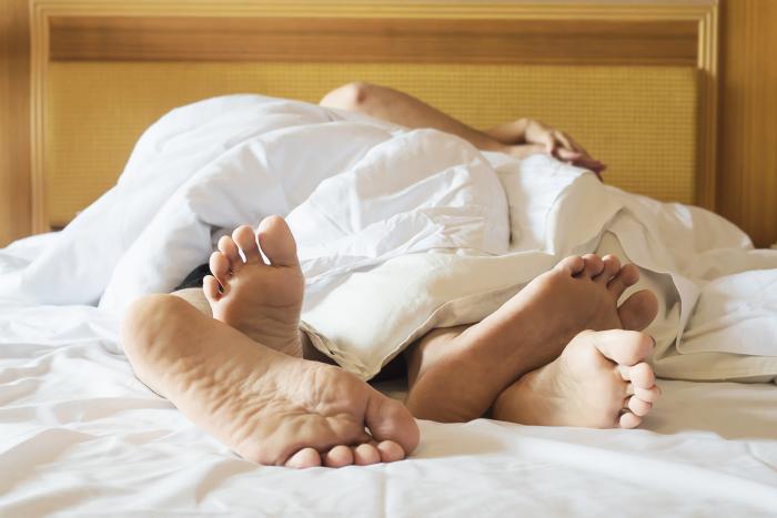 couple-on-white-bed-in-hotel-room-focus-at-feet