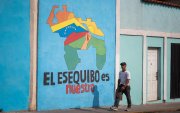 Transeúntes caminando frente a un mural con el mapa de Venezuela que dice "El Esequibo es nuestro", en Caracas.