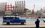Un auto viejo de transporte colectivo al pasar frente a una planta flotante de generación eléctrica en el puerto de La Habana (Cuba).