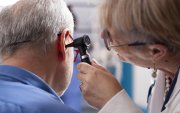 Experienced retired female physician inspecting ear of elderly male patient in clinic office. Closeup of skilled old doctor using otoscope during medical consultation of senior white man.