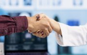 Indian general practitioner greeting her male patient at a medical examination, sharing a handshake and discussing about diagnostic reports. Woman doctor helping man to treat an illness. Close up.