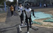 Un técnico camina detrás de un robot humanoide antes de la carrera de humanos y robots en Pekín.