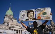 Un partidario del presidente Javier Milei, muestra un cartel de un billete de cien dólares con la imagen del presidente afuera del Congreso.