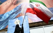 Una mujer con velo sostiene la bandera nacional de Irán frente a una enorme valla publicitaria antiestadounidense en Teherán, Irán, el 11 de mayo de 2026.