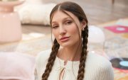 Fotografía promocional de Yami Safdie en un ambiente interior con tonos pastel. La artista aparece sentada en el piso, con trenzas, blusa blanca tejida y una estética visual vinculada al universo de Querida Yo.