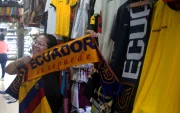 Una clienta sostiene una bufanda tricolor con el lema "Ecuador, sí se puede" en un local repleto de prendas alusivas a la selección, en plena fiebre por la moda mundialista.