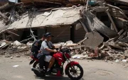 Personas transitan en motocicleta frente a edificios colapsados por los terremotos en Catia La Mar, Venezuela.