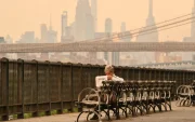 Una persona sentada en un banco lee un periódico mientras el humo de los incendios forestales provenientes de Canadá provoca una densa neblina el 16 de julio de 2026 en Nueva York.