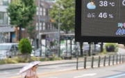 Un tablero digital muestra 38 °C en una calle de Pyongyang, mientras un transeúnte se protege del sol con sombrilla en plena ola de calor.