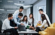 Guy shows document to a girl. Group of young freelancers in the office have conversation and working.