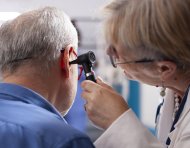 Experienced retired female physician inspecting ear of elderly male patient in clinic office. Closeup of skilled old doctor using otoscope during medical consultation of senior white man.