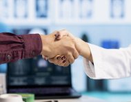 Indian general practitioner greeting her male patient at a medical examination, sharing a handshake and discussing about diagnostic reports. Woman doctor helping man to treat an illness. Close up.