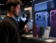 Una persona sostiene uno de los nuevos modelos de iPhone mientras observa otros dispositivos exhibidos en una tienda de tecnología.