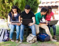 Group of teenagers social networking using several tech devices in high school
