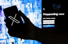 Fotografía que muestra un usuario mientras sostiene un teléfono móvil que muestra el logotipo 'X' frente a la página principal de Twitter.