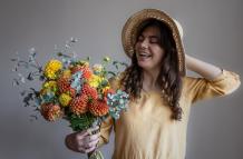 cheerful-young-woman-yellow-dress-hat-with-bouquet-bright-chrysanthemums-gray-background