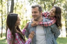 woman-looking-her-husband-carrying-their-daughter-park
