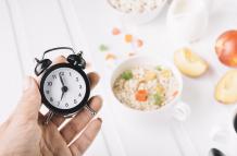 person-s-hand-holding-alarm-clock-hand-breakfast-table