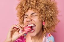 close-up-shot-cheerful-curly-haired-woman-keeps-mouth-widely-opened-bites-delicious-macaroon-enjoys-eating-sweet-food-has-sugary-addiction-isolated-pink-background-confectionery-concept