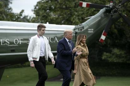 Barron Trump, de chaqueta blanca y pantalones negros, junto a sus padres Donald y Melania Trump.