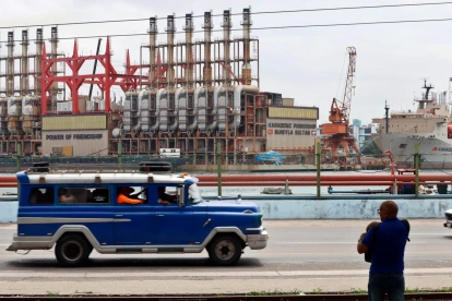 Un auto viejo de transporte colectivo al pasar frente a una planta flotante de generación eléctrica en el puerto de La Habana (Cuba).