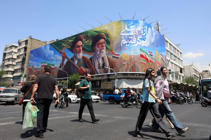 Iraníes pasan frente a una gran valla publicitaria con los difuntos líderes supremos iraníes, los ayatolás Ruhollah Jomeini y Ali Jameneí, en una calle de Teherán, Irán.
