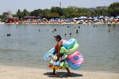 AME640. RÍO DE JANEIRO (BRASIL), 26/12/2025.- Una mujer vende flotadores y juguetes para la arena en la playa del lago artificial 'Piscinão de Ramos' este viernes, en Río de Janeiro (Brasil). El Instituto Nacional de Meteorología de Brasil (Inmet) emitió este viernes una alerta roja para todo el territorio de los estados de São Paulo y Río de Janeiro por una ola de calor que, previsiblemente, se prolongará hasta el lunes. EFE/ Antonio Lacerda