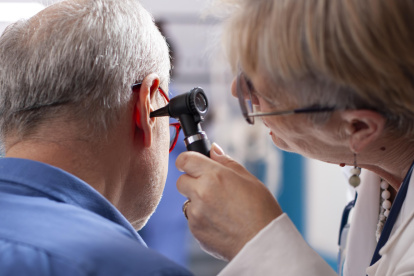 Experienced retired female physician inspecting ear of elderly male patient in clinic office. Closeup of skilled old doctor using otoscope during medical consultation of senior white man.