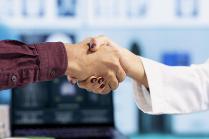 Indian general practitioner greeting her male patient at a medical examination, sharing a handshake and discussing about diagnostic reports. Woman doctor helping man to treat an illness. Close up.