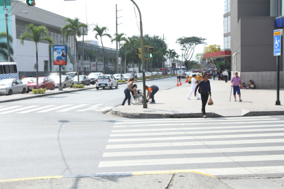 Rampas. Una mujer en silla de rueda es ayudada a subir la acera sin rampa. Al frente, una subida demasiado estrecha.