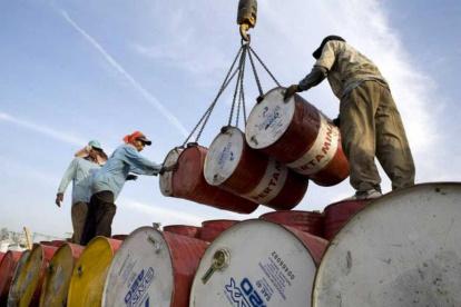 Un grupo de trabajadores mueven barriles con petróleo.