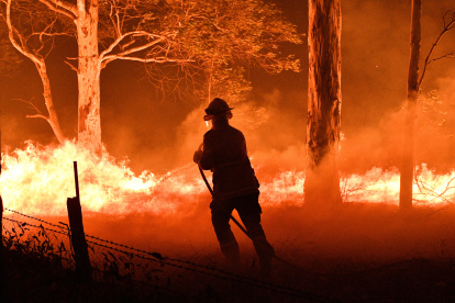 NOWRA. Un bombero intenta aplacar el fuego que consume los árboles de un bosque cercano a una zona poblada de esta ciudad del estado australiano de Nueva Gales del Sur.