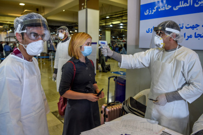 Personal de servicios de salud que usa equipo de protección verifica la temperatura corporal de un pasajero, en Kabul, por disposición de las autoridades afganas.