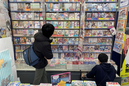 Dos personas observan algunos de los títulos de manga más populares del momento, que son también adaptados a series de anime, en una tienda de Tokio, Japón.