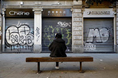 Una persona sentada frente a los locales comerciales cerrados de la vía Paolo Sarpi, conocida como el "ChinaTown" de Milán.