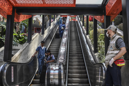 A public worker wearing a face mask as a preventive measure against the spread of the new Coronavirus, COVID-19, stands by the electrical staircases at the Comuna 13 neighborhood as healths workes pass by in Medellin, Colombia on March 16, 2020. - The Colombian government announced the indefinite suspension of face-to-face classes in public schools and universities as a preventive measure against the COVID-19 pandemic. (Photo by JOAQUIN SARMIENTO / AFP)
