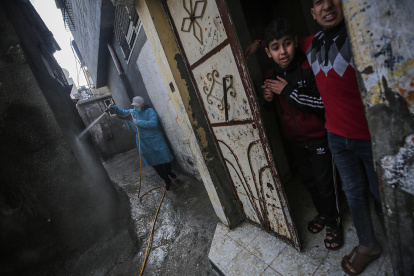 Niños palestinos observan desde la puerta de su casa como un hombre desinfecta una calle cercana este martes en Gaza, Palestina. Tanto la Autoridad Nacional Palestina, que gobierna Cisjordania ocupada, como Hamás, que controla de facto la Franja de Gaza, también han reaccionado con severidad al coronavirus, y hasta ahora se registran muy pocos casos. EFE/Mohammed Saber -FOTODELDÍA- PALESTINA CORONAVIRUS PANDEMIA COVID19