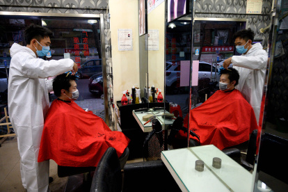 Un barbero usa un traje de bioseguridad y una mascarilla al atender a un cliente en su local en la ciudad de Wuhan.
