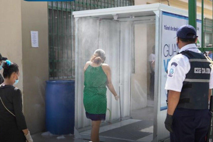 Dos personas se aprestan a pasar por el túnel de desinfección instalado en el mercado de Montebello, ubicado al norte de Guayaquil.