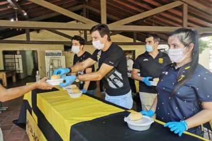 El técnico Gustavo Costas (c) durante la entrega de un guiso de pollo como parte de la iniciativa olla popular.