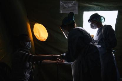 A nurse (R) and a doctor wearing personal protective equipment (PPE) in a tent on the grounds of the Sophiahemmet private hospital, perform tests on a patient to see if she has symptoms of COVID-19 on April 22, 2020 in Stockholm. - Those who are deemed not to be suffering from COVID-19 are allowed to go to a primary care centre for treatment for their condition while those who are presenting symptoms of the virus are told to return home to self-isolate or, in severe cases, sent to hospital for care (Photo by Jonathan NACKSTRAND / AFP)