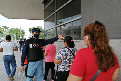 Un guardia toma la temperatura corporal a personas que quieren ingresar al Banco del Pacífico, en el Mall del Sur.