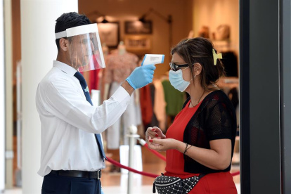Un guardia de seguridad con mascarilla mientras controla la temperatura corporal de un cliente en un centro comercial de Beirut, Líbano.