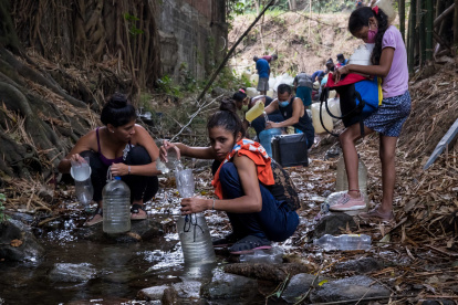 Cientos de ciudadanos recogen agua de un riachuelo.