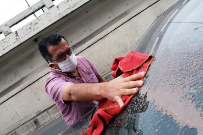 En Guayaquil, una persona retira la ceniza con un trapo húmedo; utiliza mascarilla para protegerse del COVID-19 y del polvo volcánico.