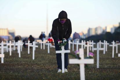 A demonstrator places flowers on a cross during a protest against Brazilian President Jair Bolsonaro and in honour of the people who died of COVID-19 in which 1000 crosses were placed in front of the National Congress in Brasilia, on June 28, 2020, amid the novel coronavirus pandemic. - The pandemic has killed at least 495,288 people worldwide, including more than 55,000 in Brazil, since it surfaced in China late last year, according to an AFP tally at 1900 GMT on Saturday, based on official sources. (Photo by Sergio LIMA / AFP)