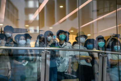 Ciudadanos con mascarilla observan a los manifestantes de una protesta contra la nueva ley de seguridad nacional para Hong Kong tras la cristalera de una tienda, el 1 de julio de 2020 en la ciudad china