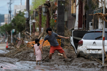 Una niña observa a su padre mientras recupera algunas de sus pertenencias tras las fuertes lluvias este miércoles en Kurume (Japón). Las precipitaciones torrenciales se extendieron hoy al centro de Japón, donde las autoridades han decretado la evacuación de más de 200.000 personas, después de dejar al menos 58 muertos en el sudoeste del país desde el fin de semana. EFE/ Kimimasa Mayama