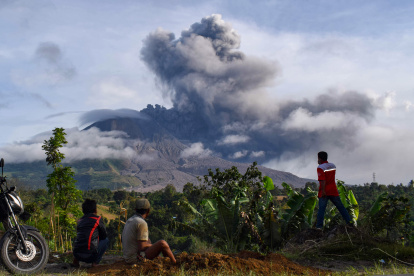 Villagers watch the eruption of Mount Sinabung as seen from Karo, North Sumatra on August 13, 2020. - Indonesia"s Mount Sinabung erupted again on August 13 with a string of blasts that sent plumes of ash two kilometres (1.2 miles) into sky, triggering a flight warning and fears of lava flows. (Photo by ANTO SEMBIRING / AFP)